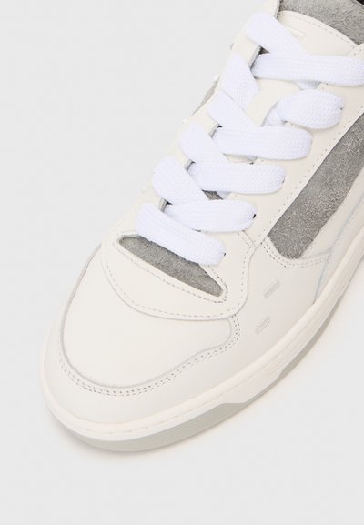 Weiße Sneaker mit dicken weißen Schnürsenkeln und grauen Wildlederdetails an der Zunge und der Seitenplatte.