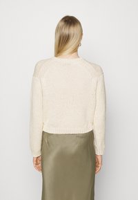 Crème, gebreide trui met een cropped ontwerp en raglanmouwen. Ribgebreide zoom en gestructureerde stof. Gecombineerd met een soepele olijfgroene rok.