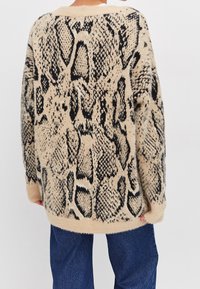 Beiger Pullover mit schwarzem Schlangenmuster, weicher Textur, oversized Schnitt, langen Ärmeln und Rundhalsausschnitt.