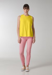 Gul ärmlös topp, lätt tyg, lös passform; ihop med åtsittande rosa byxor, slät yta, som fulländar looken med beige sneakers.