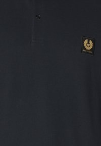 Jūras spēku stila polo krekls, kas izgatavots no teksturēta auduma, ar apkakli, vienu pogu un zelta zīmola logotipa uzšuvumu kreisajā krūtī.
