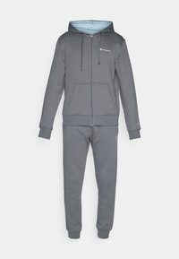 Grijze zip-up hoodie met een lichtblauwe binnenkant en voorzakken, gecombineerd met bijpassende grijze sweatpants met enkelboorden en logo-accenten.