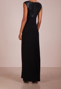 Lång svart klänning med en texturerad, glänsande bodice, ärmlös design och en figurnära silhuett, med en diskret dragkedja bak.