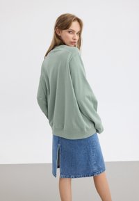 Sweat-shirt surdimensionné vert menthe avec des poignets côtelés, associé à une jupe en denim bleue présentant une fente sur le côté et des bords ourlés.