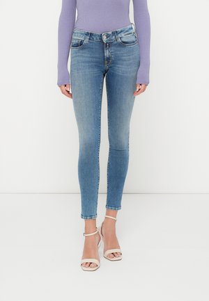 Svetlo modre skinny jeans z izbledelim vzorcem, dizajn s petimi žepi in srednjim pasom, v kombinaciji s svetlo bež sandali na vezalke.