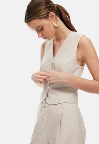 Beige gestreifter Weste mit tiefem V-Ausschnitt und einem einzigen Knopfverschluss. Verfügt über einen schlanken Schnitt und maßgeschneiderte Gestaltung, kombiniert mit einer abgestimmten Hose.