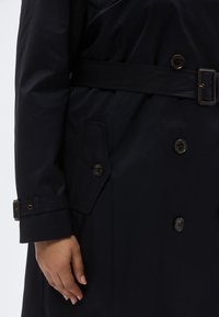 Matt sötétkék ballonkabát, derékrésznél övvel, duplagombos elülső résszel és oldalzsebbel, amelyen fedőlap található.