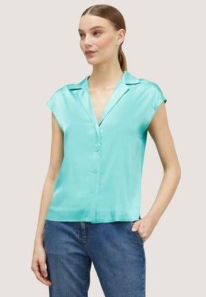 Een korte mouw, button-up shirt van glanzende turquoise satijnstof met een kraag en een relaxed fit, gecombineerd met blauwe jeans.