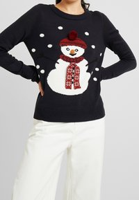 Maglione blu navy con design di un pupazzo di neve, dotato di un cappello rosso con pompon, sciarpa rossa con motivo bianco e fiocchi di neve bianchi sul davanti.