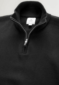 Svart zip-up-tröja med räfflad krage och textilstruktur. Har en silverdragkedja och ett varumärkesmärke vid halsen.