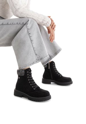 Botas de tobillo de ante negro con diseño de cordones, collar de piel de fur gris y cremallera lateral. Suela gruesa de goma con dibujo para tracción y estabilidad.
