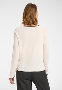 Helles beige Sweatshirt mit langen Ärmeln, einem runden Halsausschnitt und schwarzem Besatz. Verfügt über Knopfdetails an den Bündchen. Weicher, leichter Stoff.
