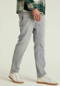 Jeans gris claro con corte ajustado, que cuentan con bolsillos laterales y un ligero desgaste. Combinados con zapatillas blancas y una camisa de cuadros verde.