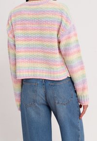 Pull au style crochet avec des rayures pastel en rose, bleu et jaune ; design court ; texture côtelée ; associé à un jean bleu clair.