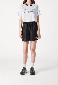 White short-sleeve sports jersey with navy accents and "SWOOSH" text, paired with black shorts featuring elastic waist and logo detail.