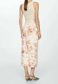 Slonovinová tílko spárované s květinovou midi sukní s růžovými a zlatými květinami na světlém pozadí. Sandály na tenkých podpatcích, zelené.