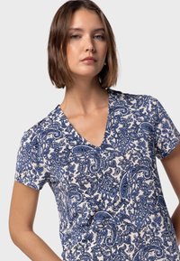 Kortärmad V-ringad topp i vitt med ett blått paisleymönster, med en lättviktsmaterial och en avslappnad passform.
