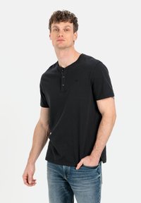 Sort kortærmet henley skjorte med tre knapper ved stolpen, lavet af blød bomuld. Båret med lyseblå jeans, let meleret tekstur.