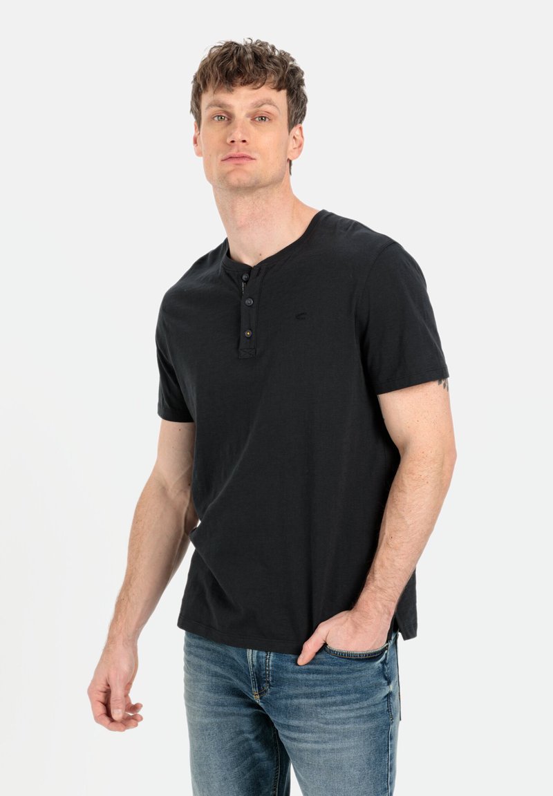 Sort kortærmet henley skjorte med tre knapper ved stolpen, lavet af blød bomuld. Båret med lyseblå jeans, let meleret tekstur.