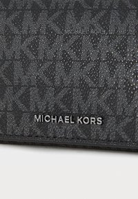 Portefeuille noir texturé avec un motif géométrique, arborant un logo métallique "MICHAEL KORS". Fabriqué en matériau synthétique, au design compact.