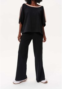 Haut noir à large encolure avec des accents beiges contrastants, associé à un pantalon noir évasé et des baskets blanches. Tissu lisse et coupe décontractée.