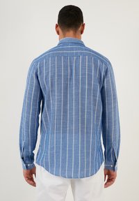 Camicia a maniche lunghe di colore azzurro chiaro con righe verticali bianche, dotata di colletto classico, polsini abbottonati e orlo arrotondato.
