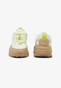 Calzado Lacoste con un upper de color amarillo claro y acentos en beige, suela texturizada y detalles en verde neón en el talón y la lengüeta.