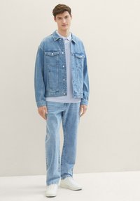 Ljusblå denimjacka med två bröstfickor, kombinerad med en ljusblå t-shirt och ljusblå jeans. Vita sneakers fulländar outfiten.