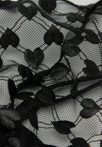 Schwarzer transparenter Stoff mit bestickten Samtherz- und Blattmotiven auf feinem Netzstoff.