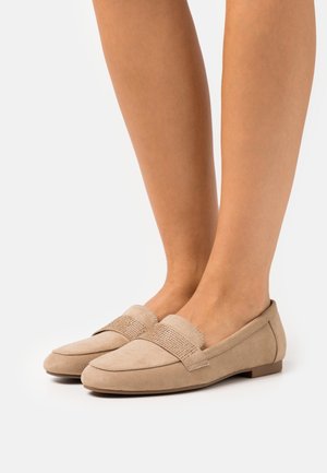 Mocasines de ante beige con una banda texturizada que presenta brillantitos. Punta redondeada y suela plana. Diseñados para la comodidad y el uso casual.