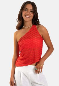 Top rojo de un solo hombro con rayas texturizadas y onduladas. Tejido ligero. Combinado con pantalones blancos y acentos de joyería simples.