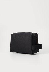 Svart stoffpose med rektangulær form, glatt tekstur og glidelås på toppen. Har et sidehåndtak for enkel bæring.