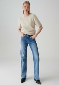 Pull en maille texturée crème à manches courtes, associé à un jeans droit bleu clair. Une ceinture noire et des bottines complètent la tenue.