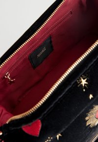 Black velvet handbag with gold star and heart embroidery, opening to a maroon fabric interior with a zippered pocket inside.