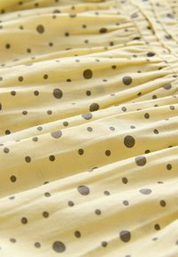 Żółty materiał w czarne kropki, z marszczoną teksturą. Gładki, lekki materiał o subtelnym połysku.