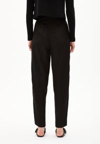 Black tailored pants featuring a high waist, pleats, and a sleek design, paired with black slip-on shoes against a neutral background.