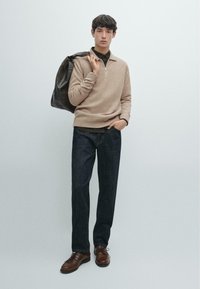 Beżowy sweter z dzianiny z półzamkiem, ciemne jeansy z denimu, brązowe skórzane buty i skórzana torba na ramię. Prosty, nowoczesny design ogólnie.