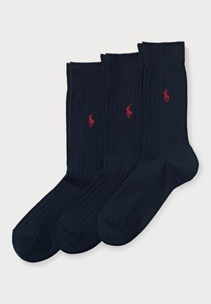 Chaussettes côtelées bleu marine avec une texture unie, arborant un petit logo rouge sur trois paires. Conçues avec une bande rembourrée en haut.