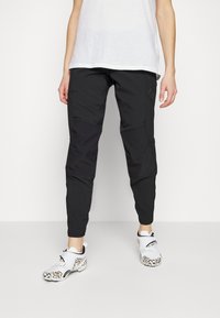 Zwarte sportbroek met taps toelopende benen, voorzien van een soepele textuur en contrasterende paneeldetails. G gedragen met witte schoenen met luipaardprintaccenten.