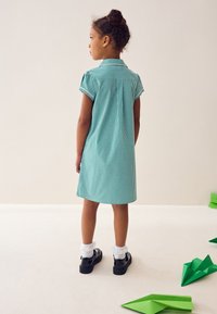 Grøn og hvid gingham-kjole med korte ærmer og krave, med rygstykke og plisseeffekt. Kombineret med sorte sko og hvide sokker.