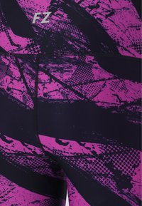 Närbild av lila och svarta träningsleggings med abstrakt splatter- och prickmönster, med "FZ"-logotypen nära midjebandet.