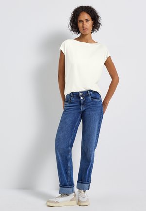 Haut blanc à manches courtes associé à un jean en denim bleu. Les baskets présentent des accents beige et blanc. Tissu lisse avec une coupe décontractée.