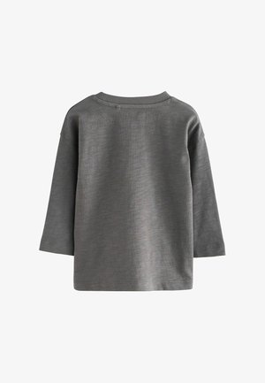 Pilkas ilgas rankovės marškinis, pagamintas iš minkštos, tekstūruotos medžiagos. Yra apvalaus kaklo su raišteliu ir nepuoštas nugaros dizainas.