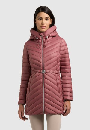 Naine kannab lavendlivärvi tikitud sulejopet kapuutsiga, vöökohaga ja esikinnitusega, seistes helehalli ühevärvilise tausta ees.