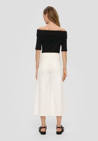 Czarny top bez ramiączek z krótkimi rękawami, zestawiony z szerokimi białymi dżinsami z tylnymi kieszeniami i postrzępionym dołem, noszony z czarnymi sandałami.