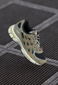 Sapato de corrida com parte superior em malha nas cores oliva e taupe, com uma sola acolchoada e detalhes bem acabados. Os atacadores são em um tom neutro.