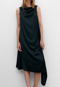 Robe sans manches noire en tissu lisse semblable à du satin, présentant une encolure à godets et un ourlet asymétrique avec un côté drapé.