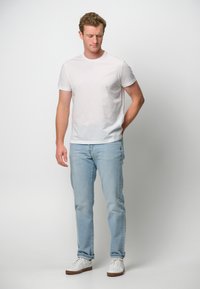 Maglietta bianca a maniche corte abbinata a jeans azzurri chiari e sneaker bianche. L'outfit presenta una vestibilità classica e un design casual.