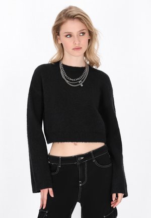 Zwarte cropped trui met lange mouwen, gemaakt van zachte, gestructureerde stof. Gecombineerd met zwarte high-waisted broeken met witte stikdetails.