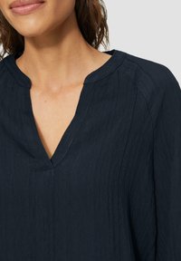 Blouse bleu marine, texturée, avec un décolleté en V et un subtil motif côtelé. Dotée de manches courtes et d'une coupe décontractée.